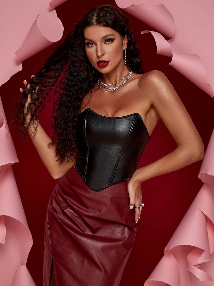 Women's black strapless PU bustier crop top featuring a lace-up back, grommet eyelet details, and an asymmetrical handkerchief hem.