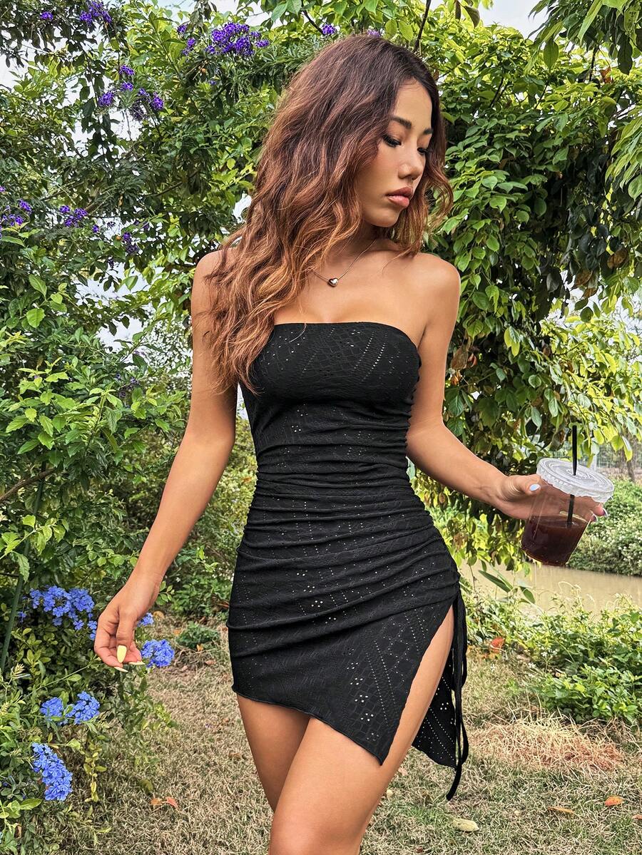 Woman wearing a black strapless ruched bodycon mini dress featuring side drawstring and split thigh details.
