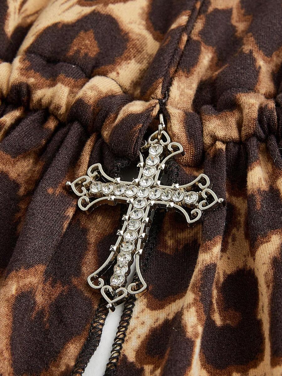 A women wearing a black halter crop top with a shiny rhinestone cross pendant, neck strap, backless cut, and asymmetrical ring detail.