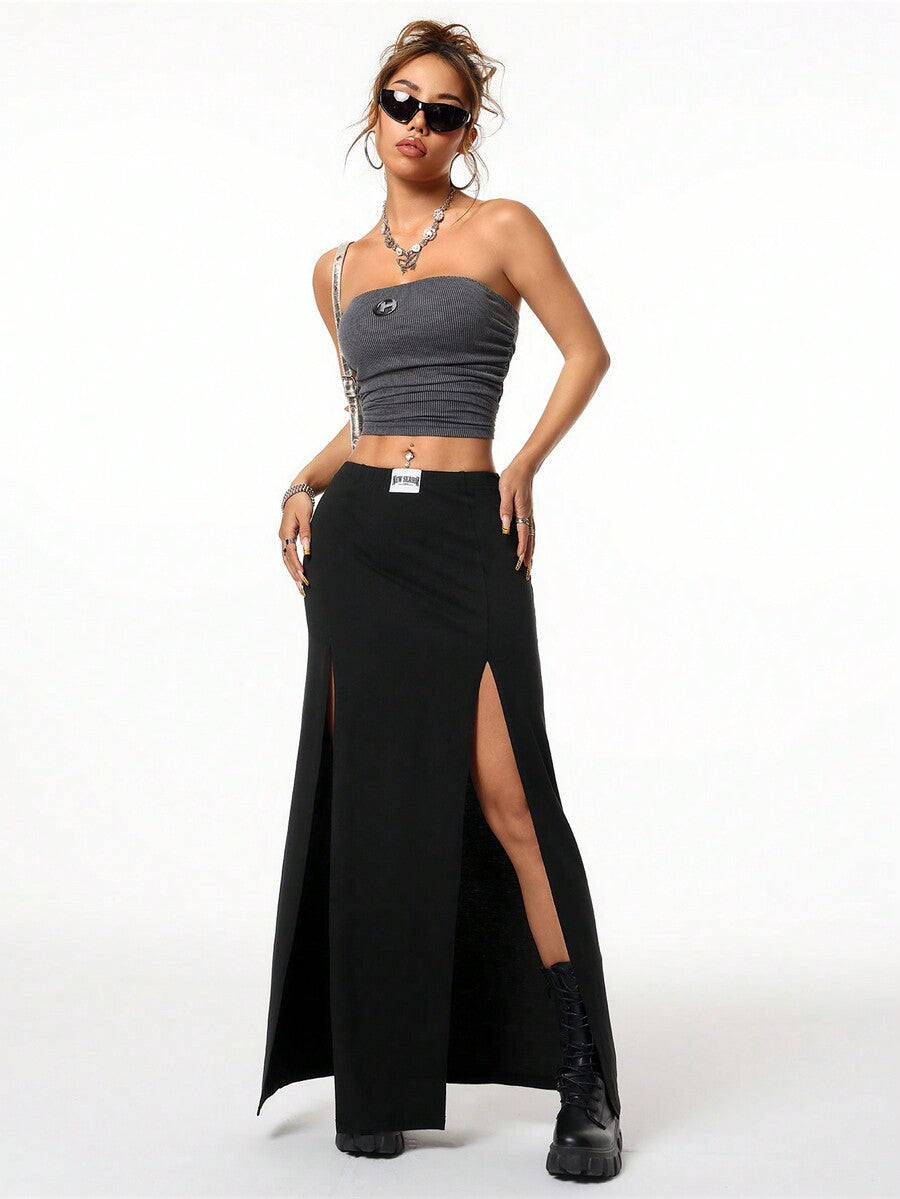 Women's black high waist long skirt with split thigh slit, zipper, and letter patch detail made from knitted stretch fabric.