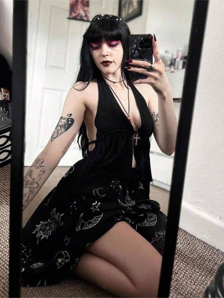 A women wearing a black halter crop top with a shiny rhinestone cross pendant, neck strap, backless cut, and asymmetrical ring detail.