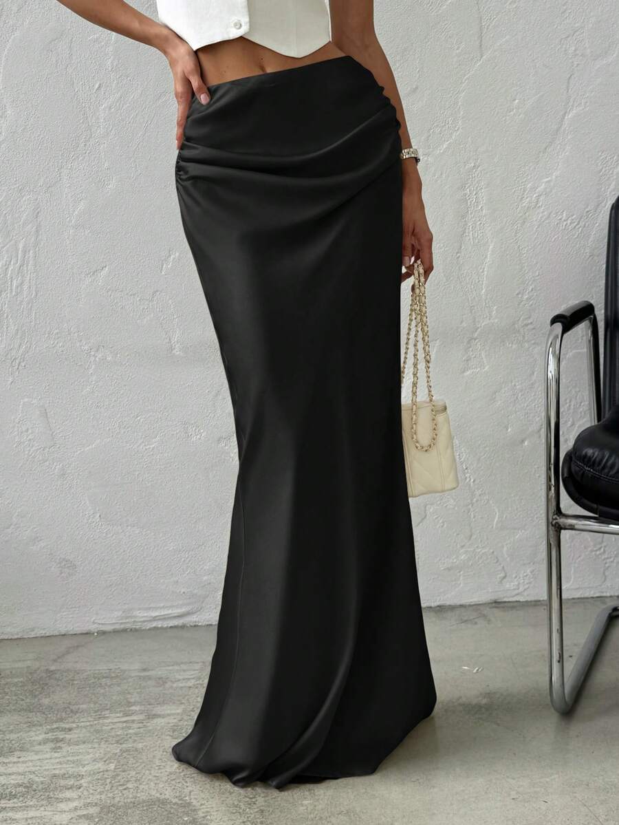 Women's black solid satin maxi skirt featuring an asymmetrical ruched design, ultra low waist, straight fit, and zipper closure.