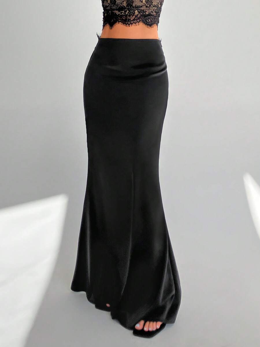 Front view of a woman wearing an elegant black satin lace patchwork bodycon fishtail maxi skirt featuring an ultra low waist and side slit detail.