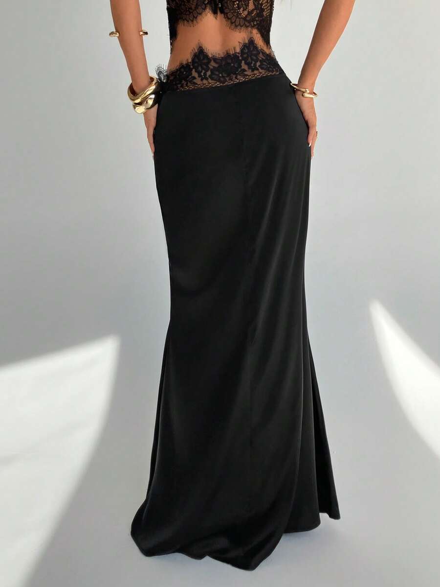 Front view of a woman wearing an elegant black satin lace patchwork bodycon fishtail maxi skirt featuring an ultra low waist and side slit detail.