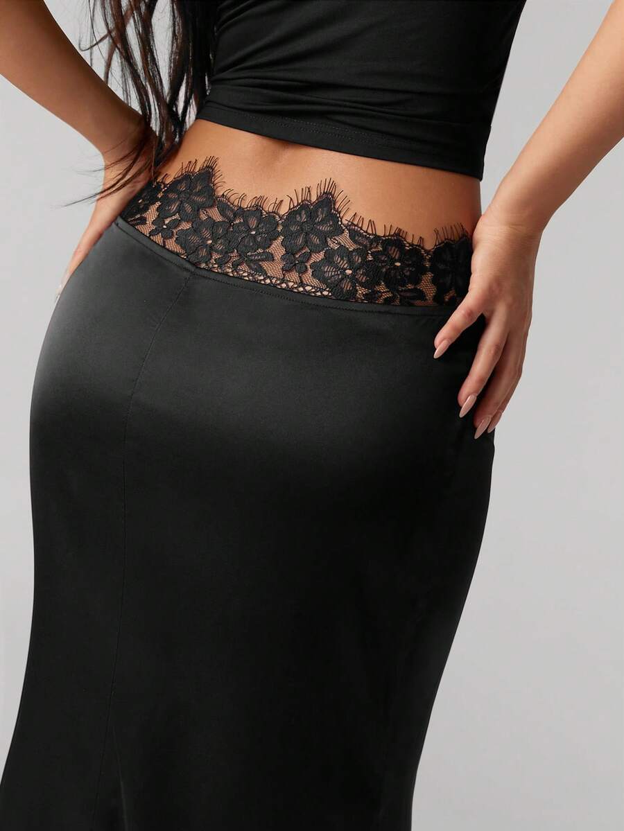 Front view of a woman wearing an elegant black satin lace patchwork bodycon fishtail maxi skirt featuring an ultra low waist and side slit detail.