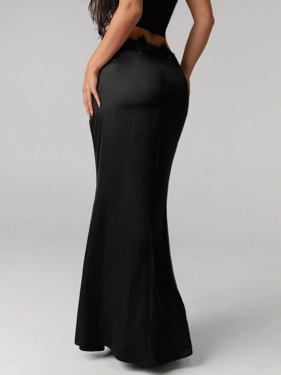 Front view of a woman wearing an elegant black satin lace patchwork bodycon fishtail maxi skirt featuring an ultra low waist and side slit detail.
