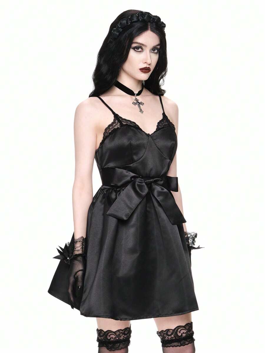 Front view of women wearing black gothic satin mini dress with contrast lace trim, bow accent, spaghetti straps, high waist, and tiered flared hem.