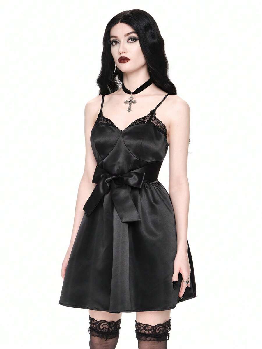 Front view of women wearing black gothic satin mini dress with contrast lace trim, bow accent, spaghetti straps, high waist, and tiered flared hem.
