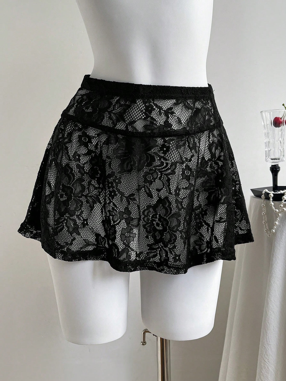 Women's black semi-sheer knitted lace mini skirt featuring a flared ruffle hem and low waist design
