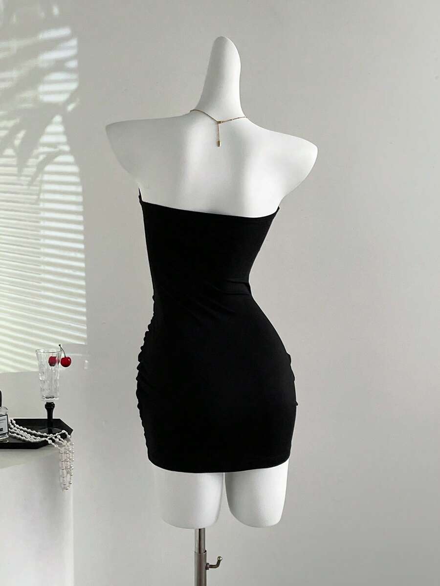 Women's black strapless bodycon mini dress featuring ruched detailing, cut-out design with ring accent, mid-waist pencil hem, and slim fit knitted stretch fabric.