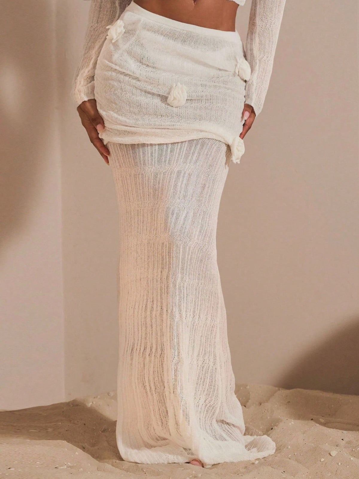 Beige women's knit maxi skirt featuring a pleated 3D floral pattern, low waist, skinny fit, and fishtail hem.