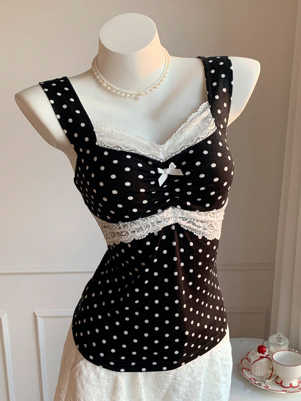 Black and white polka dot knit camisole tank top featuring delicate contrast lace trim, a cute bow accent at the sweetheart neckline, and slender shoulder straps.
