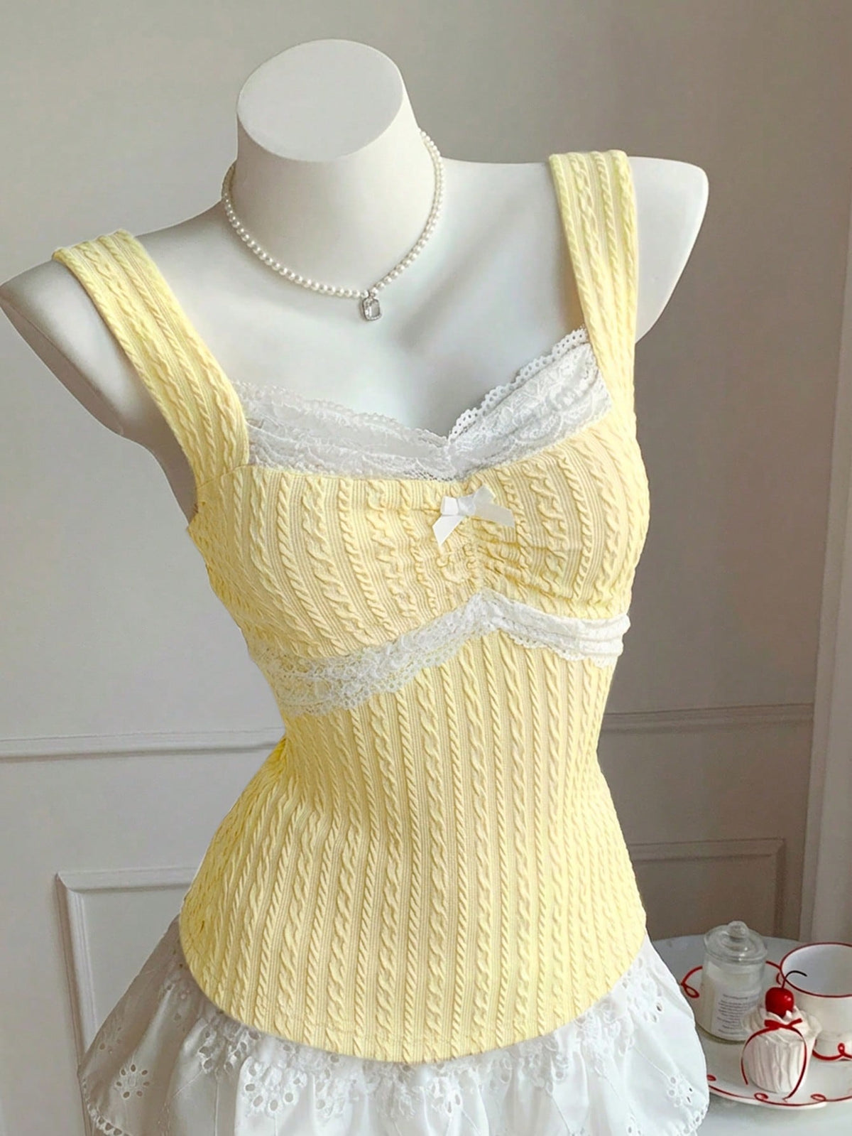 Black and white polka dot knit camisole tank top featuring delicate contrast lace trim, a cute bow accent at the sweetheart neckline, and slender shoulder straps.