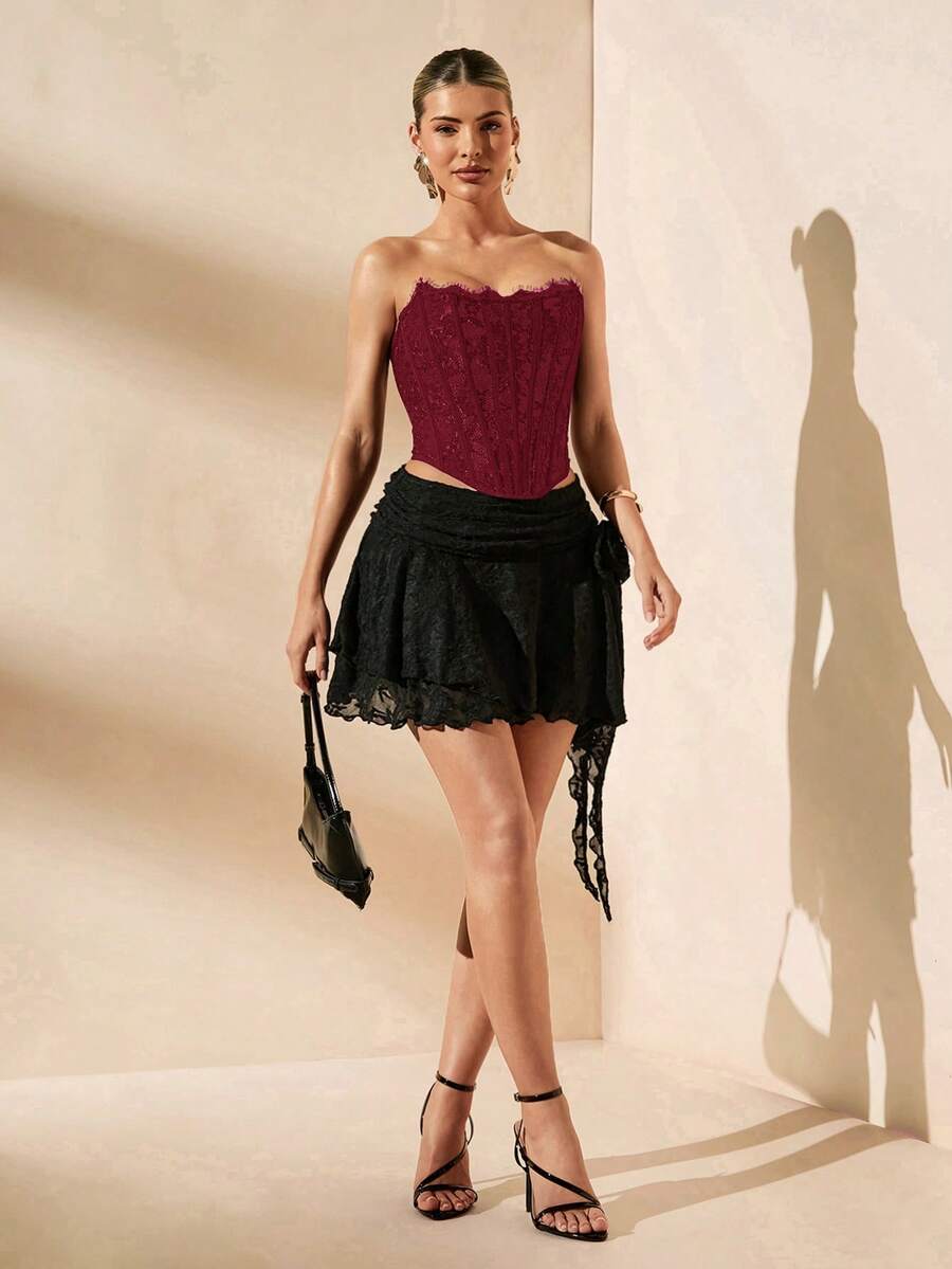 Women's strapless bustier crop top with contrast lace, lace-up detail, and an asymmetric hem in a slim-fit satin finish.
