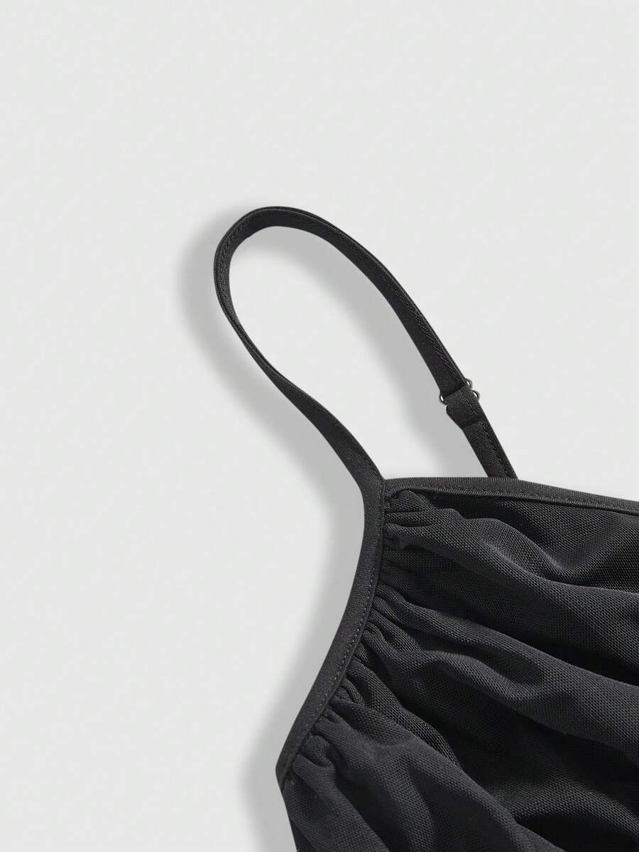 Women's black slim-fit camisole top featuring ruched body design, decorative chain accent, ruffle hem, and cold-shoulder spaghetti straps.