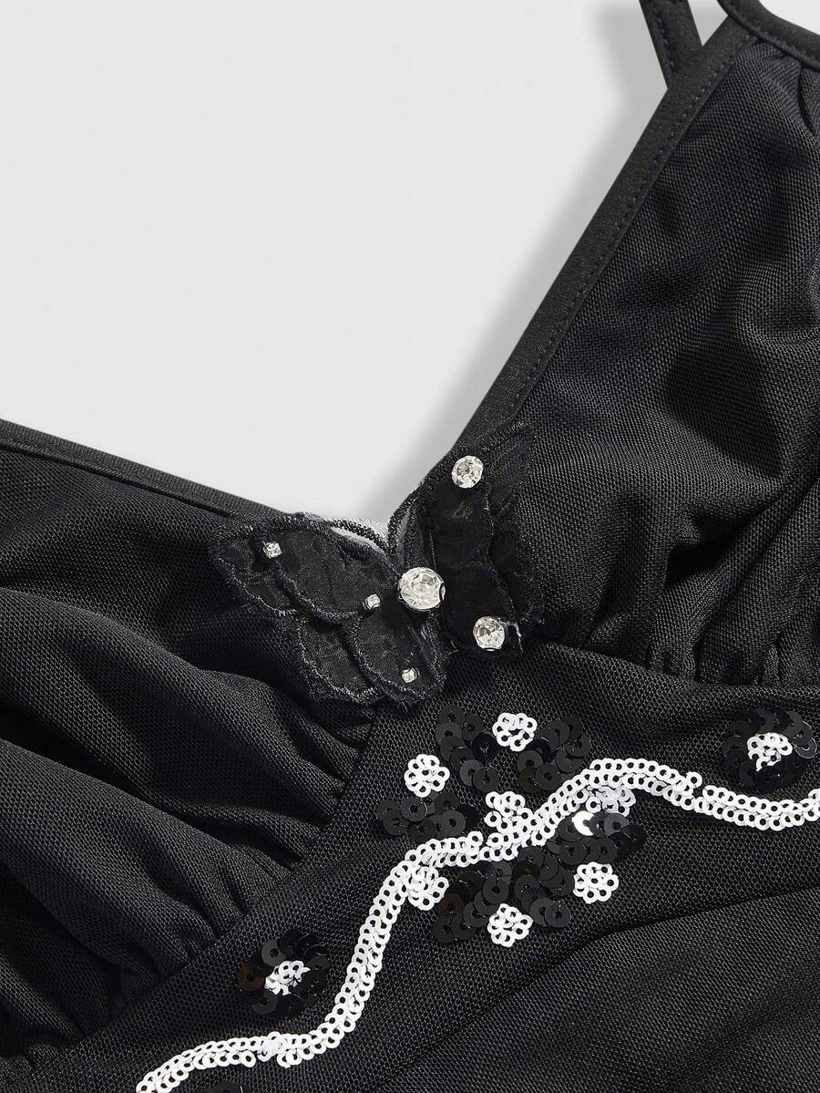 Women's black slim-fit camisole top featuring ruched body design, decorative chain accent, ruffle hem, and cold-shoulder spaghetti straps.