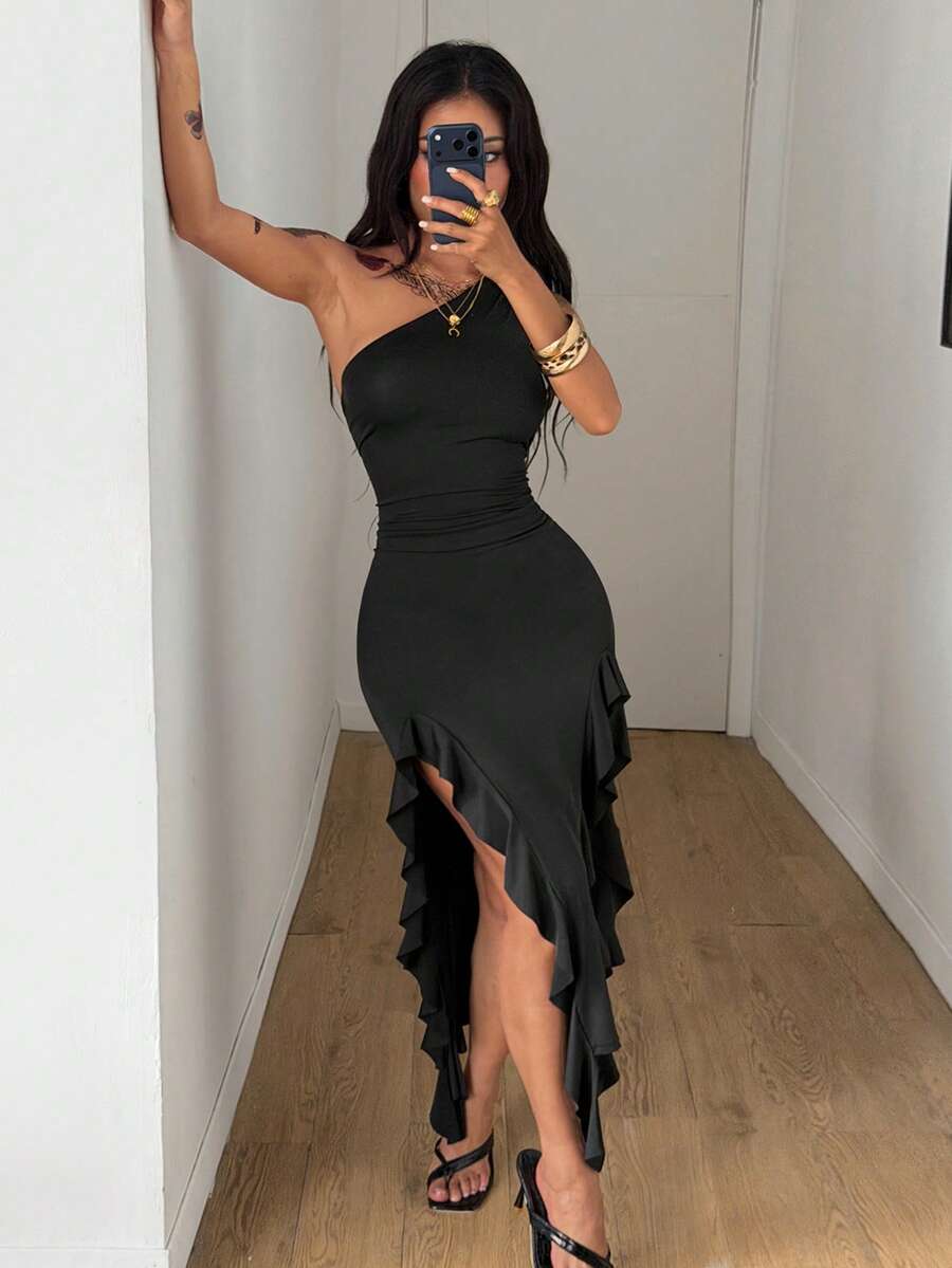 Black sleeveless asymmetrical bodycon long dress with ruffle detailing and a split thigh on a model.