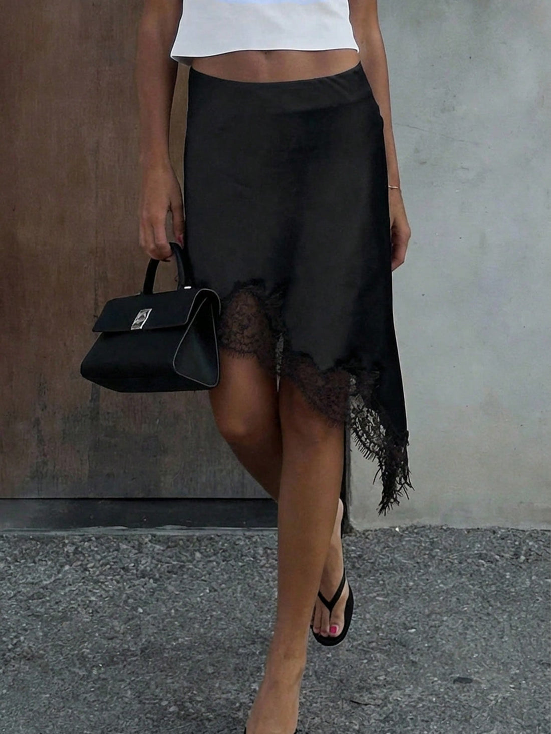 Women's black low-waist midi skirt featuring contrast lace patchwork details and an asymmetrical hemline.