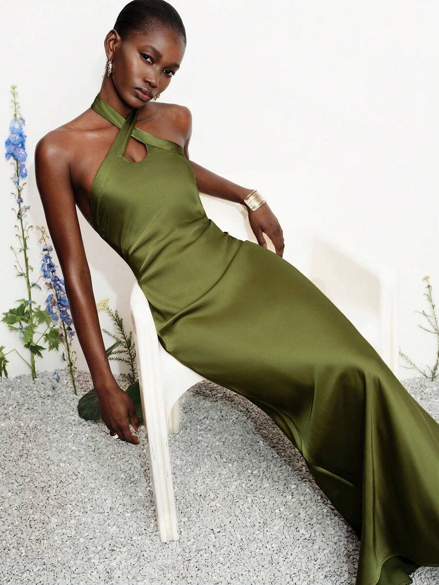 Women's black satin halter neck bodycon midi dress featuring a sleeveless backless design with front slit hem and wrap details.