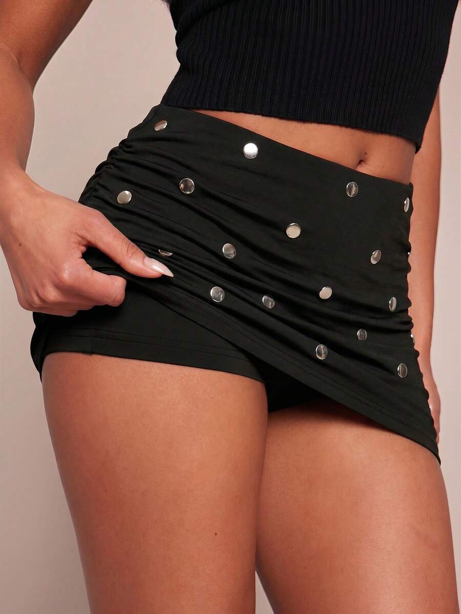 Women's black bodycon mini skort featuring a low waist, pleated side split hem, zipper closure, and built-in shorts.
