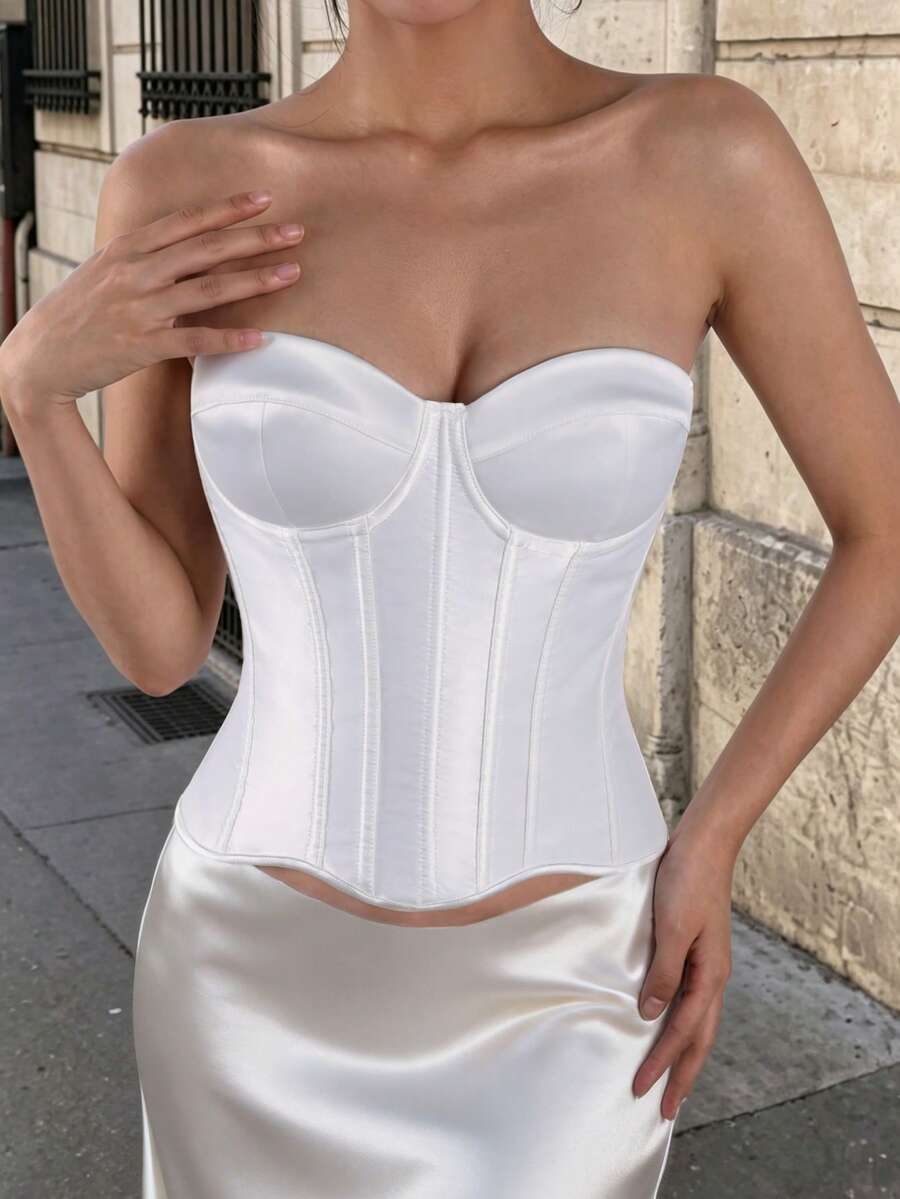 White women’s corset top with metal eyelet details, boning structure, spaghetti straps, backless tie-back design, and a slim cropped fit.