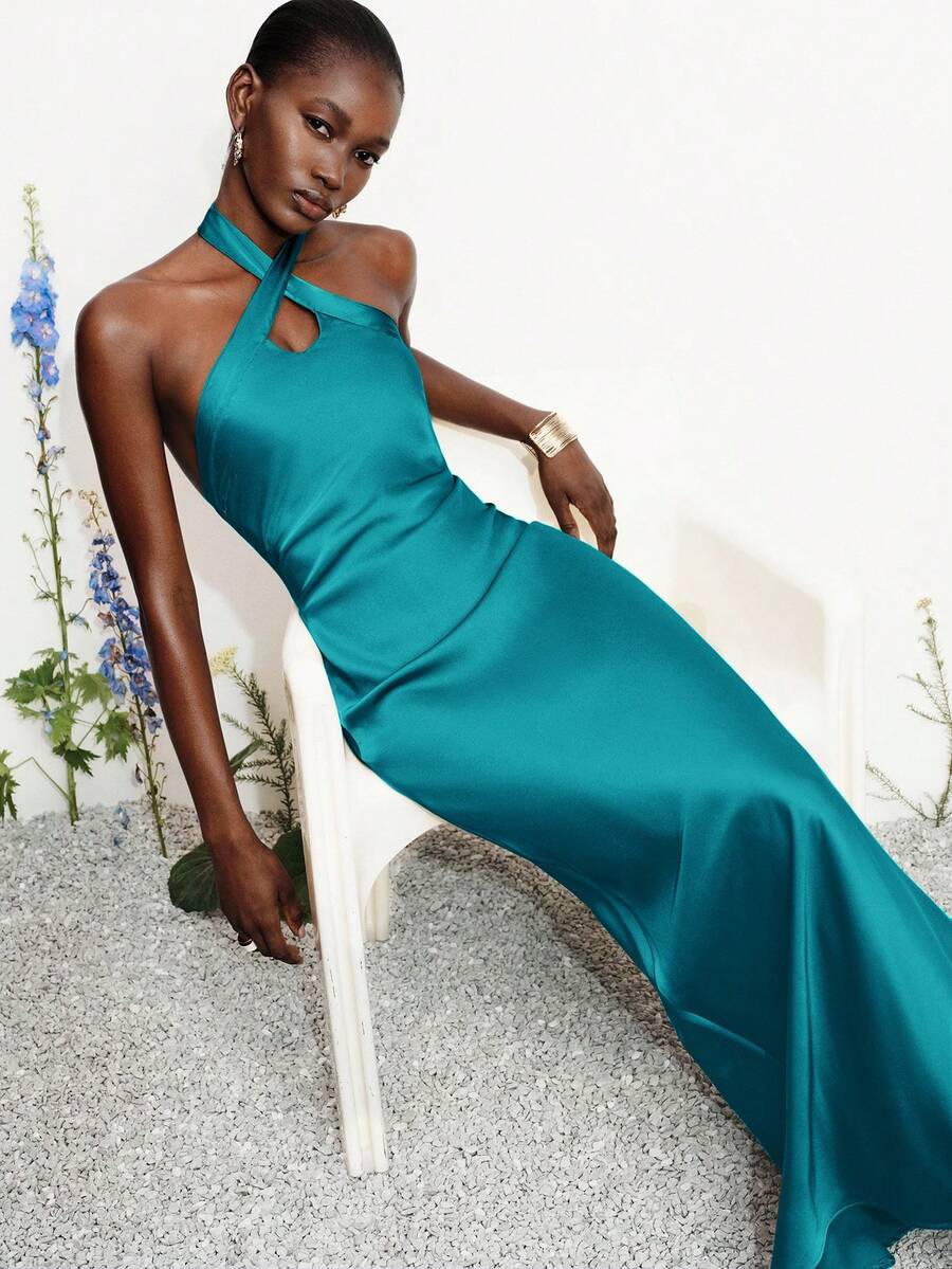 Women's black satin halter neck bodycon midi dress featuring a sleeveless backless design with front slit hem and wrap details.