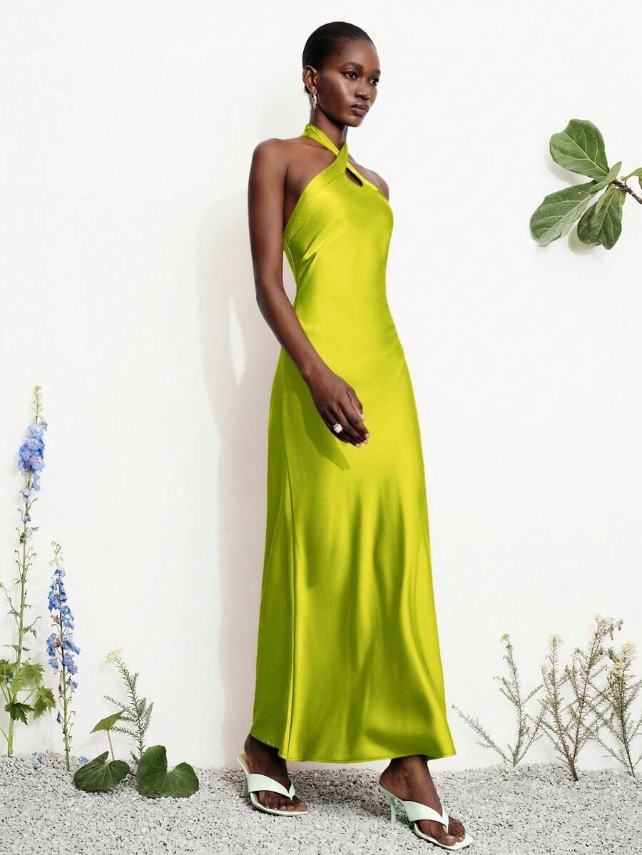 Women's black satin halter neck bodycon midi dress featuring a sleeveless backless design with front slit hem and wrap details.