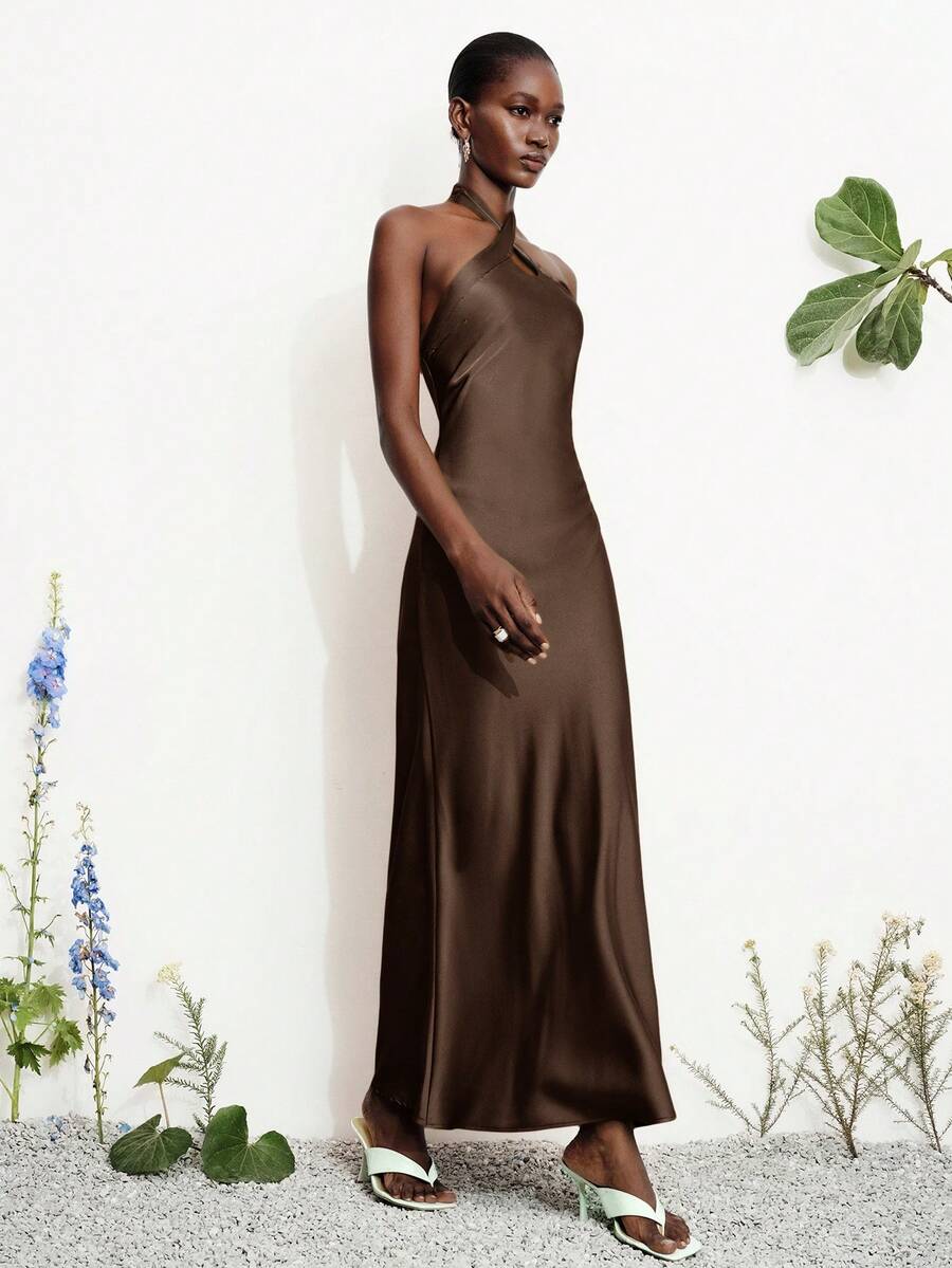 Women's black satin halter neck bodycon midi dress featuring a sleeveless backless design with front slit hem and wrap details.