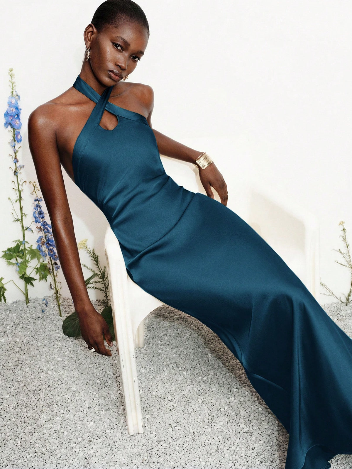 Women's black satin halter neck bodycon midi dress featuring a sleeveless backless design with front slit hem and wrap details.