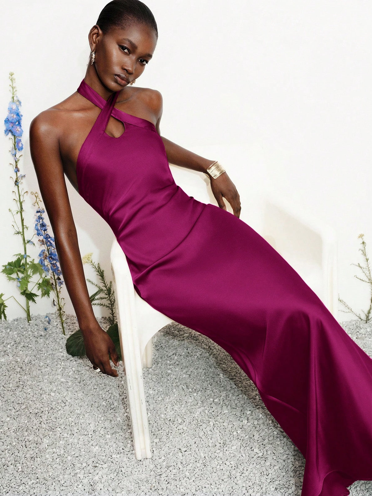 Women's black satin halter neck bodycon midi dress featuring a sleeveless backless design with front slit hem and wrap details.