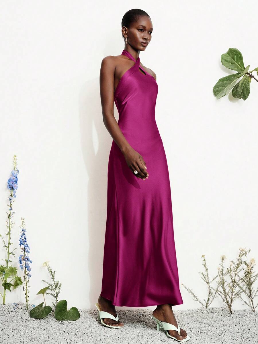 Women's black satin halter neck bodycon midi dress featuring a sleeveless backless design with front slit hem and wrap details.