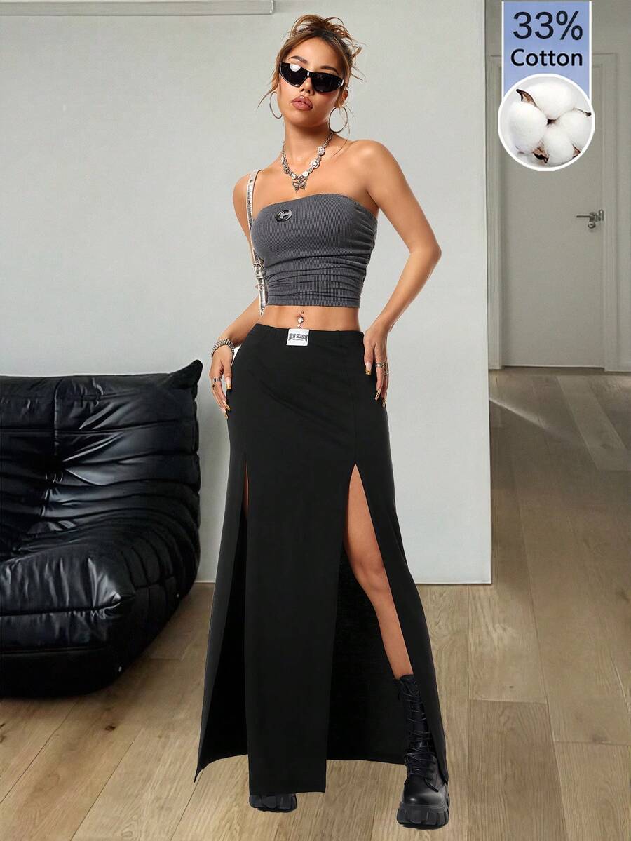 Women's black high waist long skirt with split thigh slit, zipper, and letter patch detail made from knitted stretch fabric.