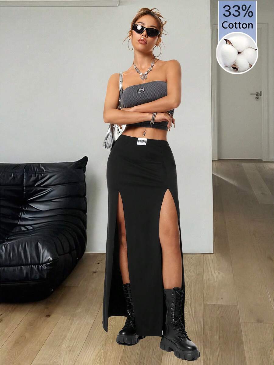 Women's black high waist long skirt with split thigh slit, zipper, and letter patch detail made from knitted stretch fabric.
