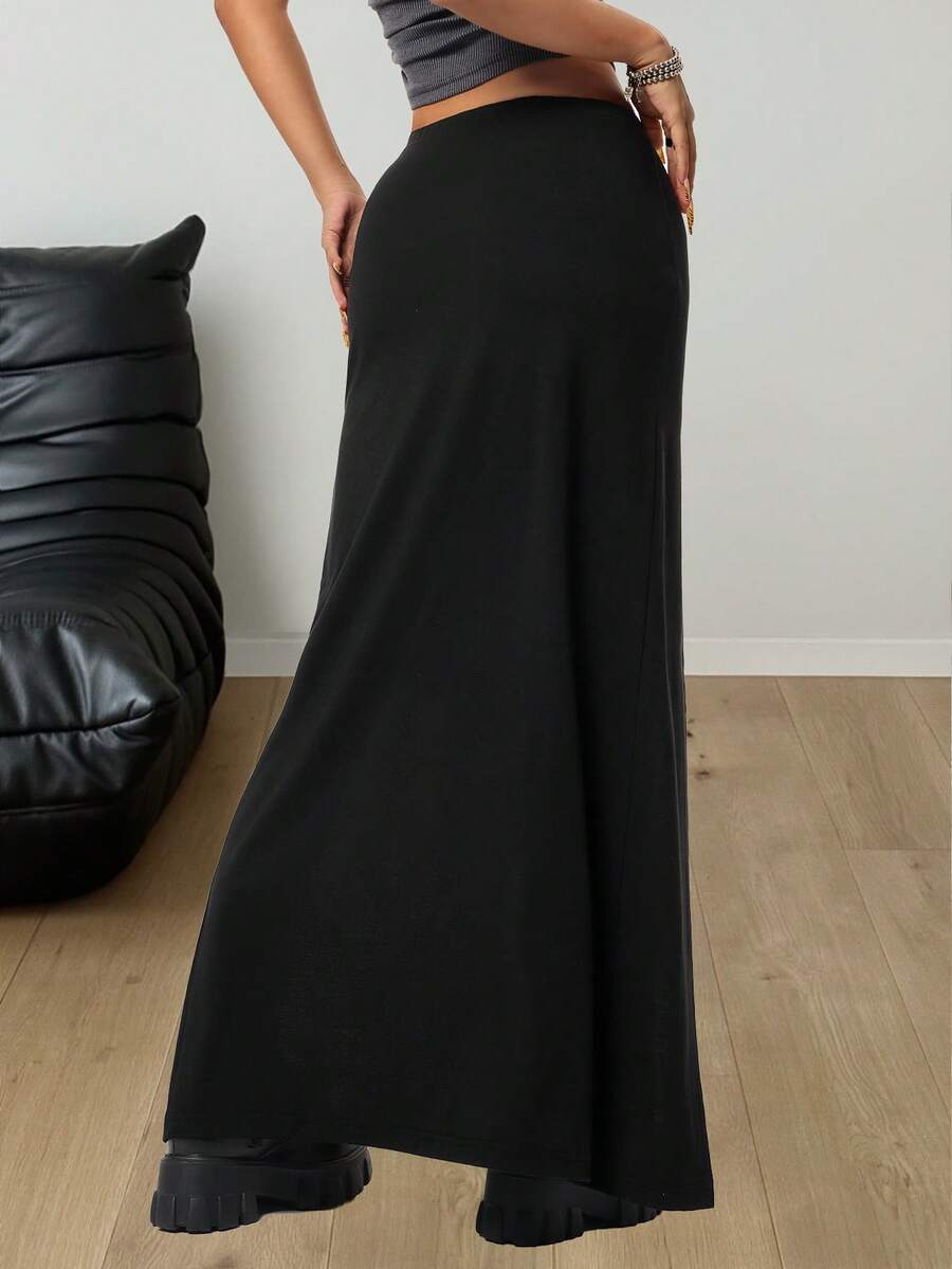 Women's black high waist long skirt with split thigh slit, zipper, and letter patch detail made from knitted stretch fabric.