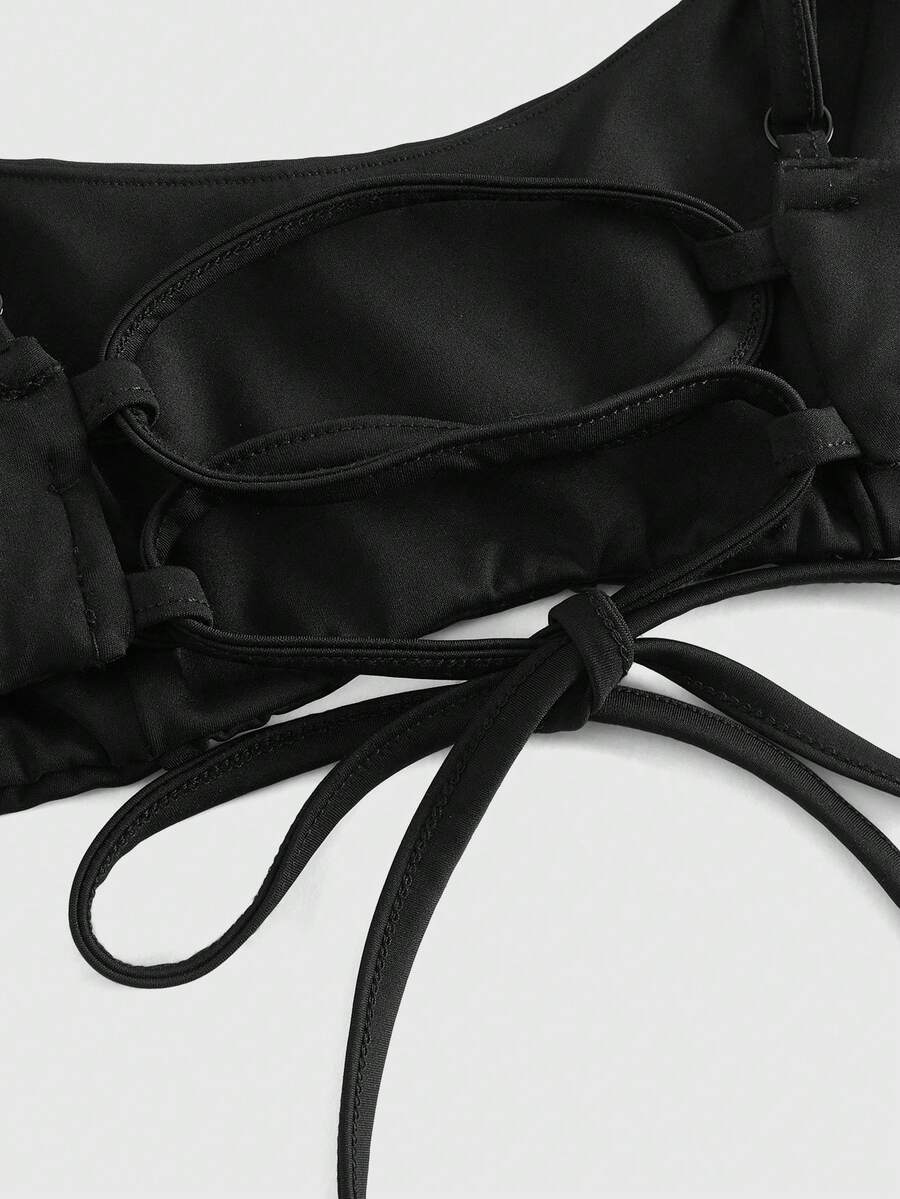 Black micro crop camisole bra featuring spaghetti straps, criss-cross ruched front detailing, and an asymmetrical hem.