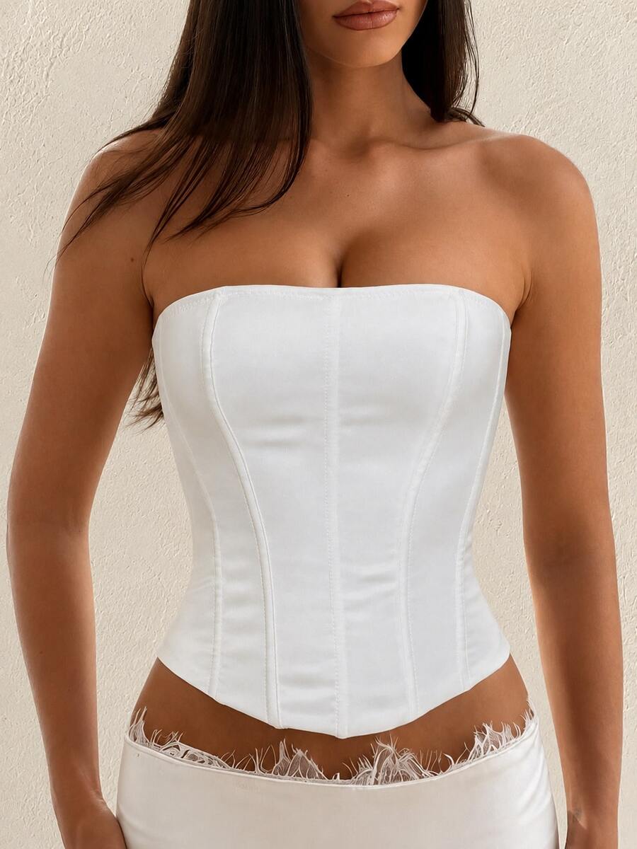 White strapless satin corset crop top for women featuring internal boning, a lace-up backless detail, and an asymmetrical hem.