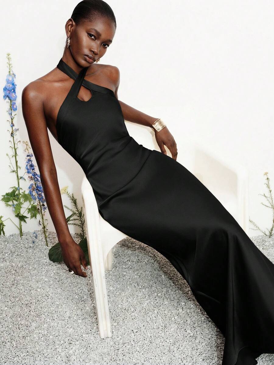 Women's black satin halter neck bodycon midi dress featuring a sleeveless backless design with front slit hem and wrap details.