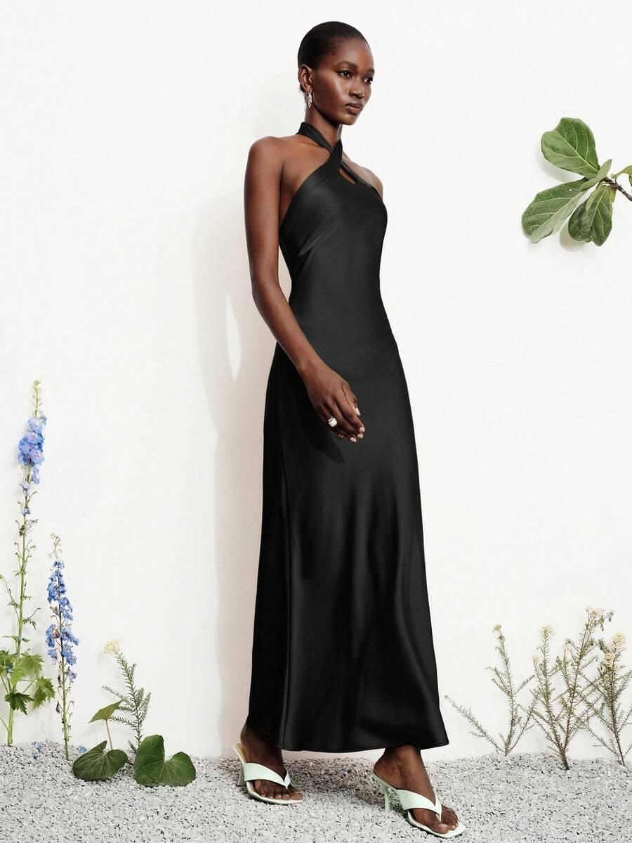 Women's black satin halter neck bodycon midi dress featuring a sleeveless backless design with front slit hem and wrap details.