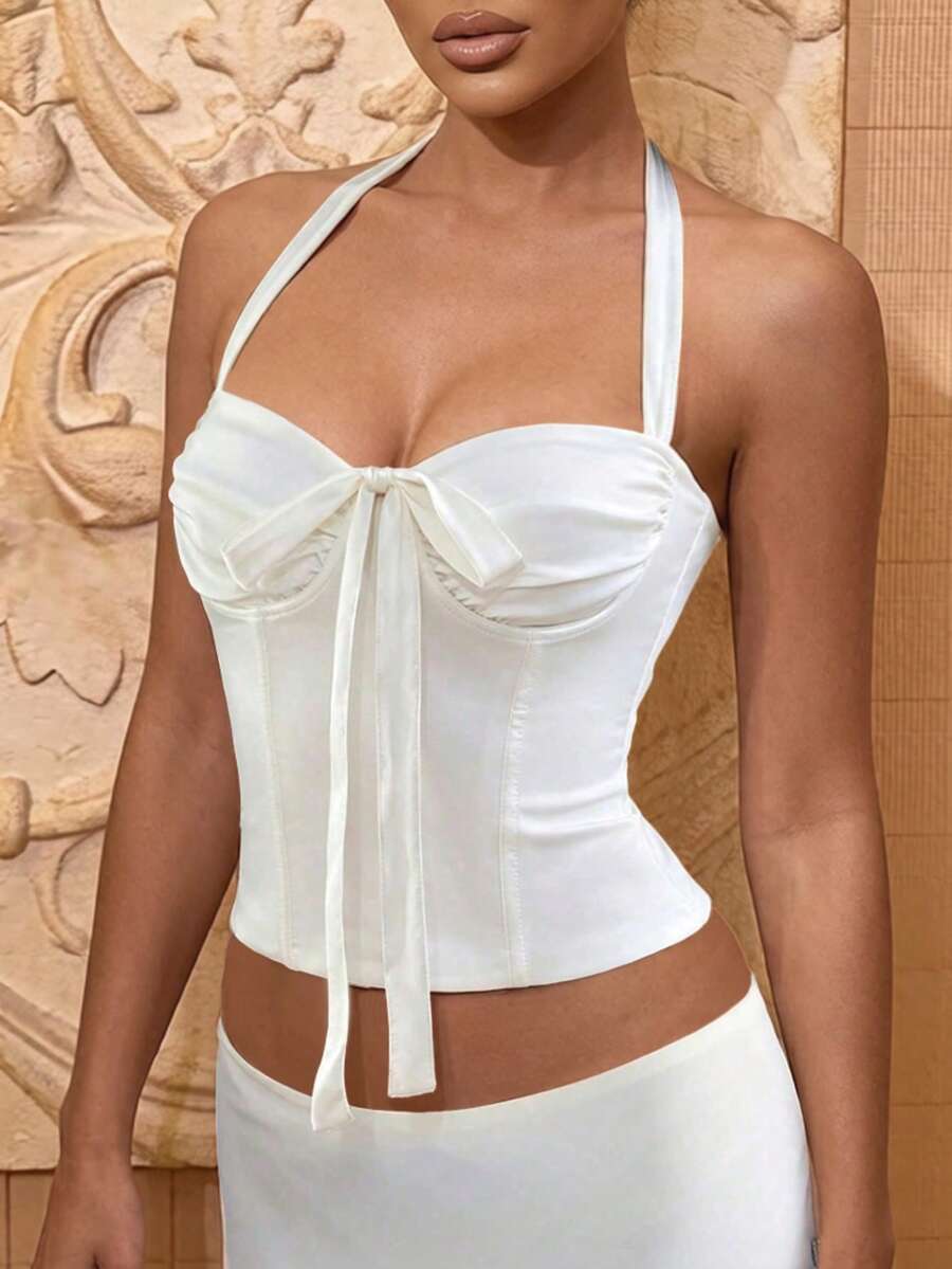 Front view of a white fitted halter corset crop top with bow tie detail and backless design for women.