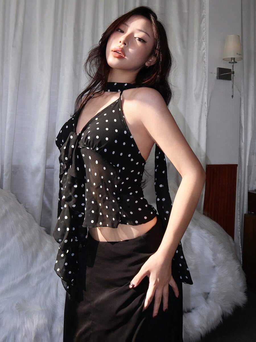 Multicolor polka dot halter crop camisole featuring a ruffle hem, backless asymmetrical design, and slim fit semi-sheer fabric on a model.