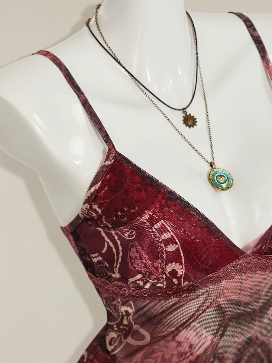Women's burgundy floral graphic print mesh camisole top featuring an asymmetrical hem, backless cut, and spaghetti straps.