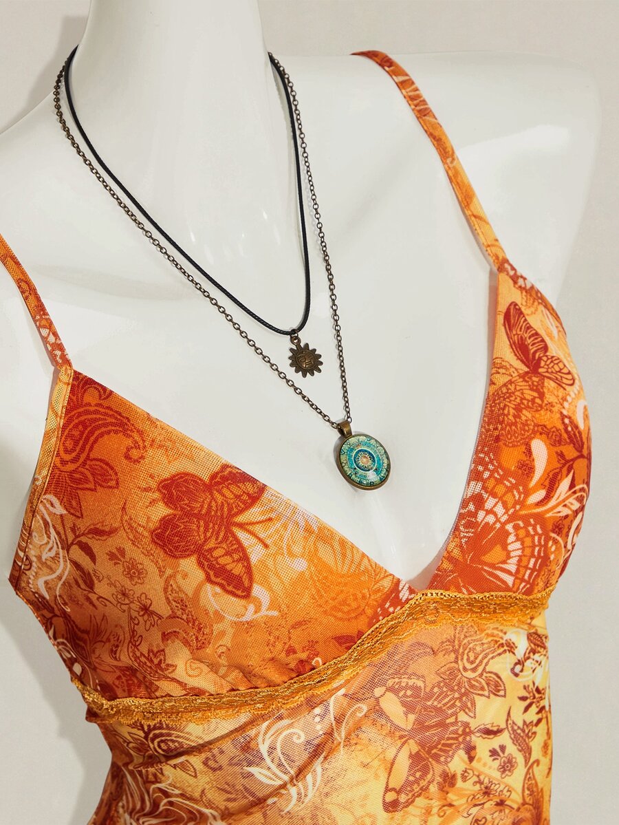 Women's burgundy floral graphic print mesh camisole top featuring an asymmetrical hem, backless cut, and spaghetti straps.